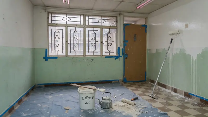 香港住宅油油工序：滾筒上乳膠漆，牆身一半批灰一半已油，地面鋪藍色保護膠紙